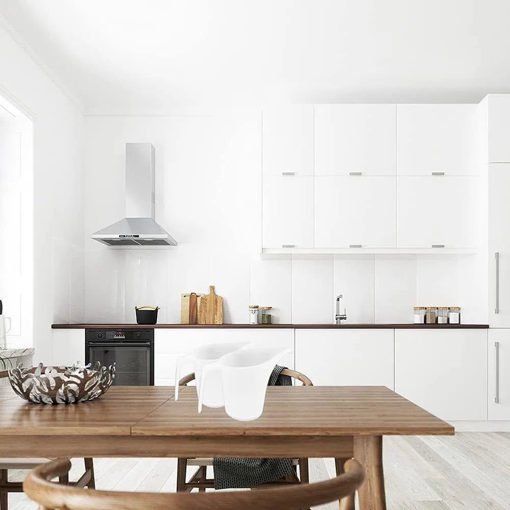 A wooden table with white ceramic pitchers and measuring tools set against a modern kitchen backdrop.