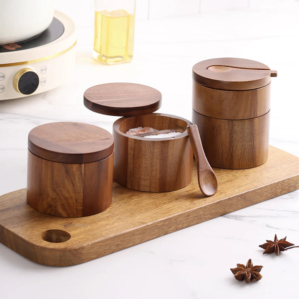 A set of wooden salt and spice jars with lids displayed on a cutting board.