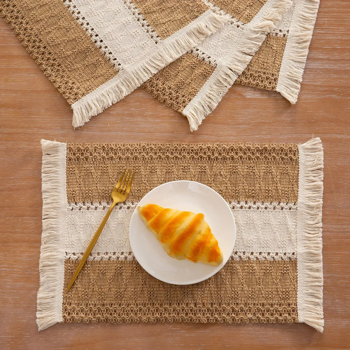 Set natürliche Jute-Platzsets mit weißen Fransen, zeigen einen Teller mit goldenen Croissants und einer Gabel.