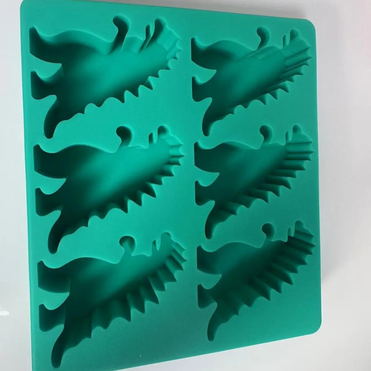 A green silicone ice cube tray set molded into dinosaur shapes.