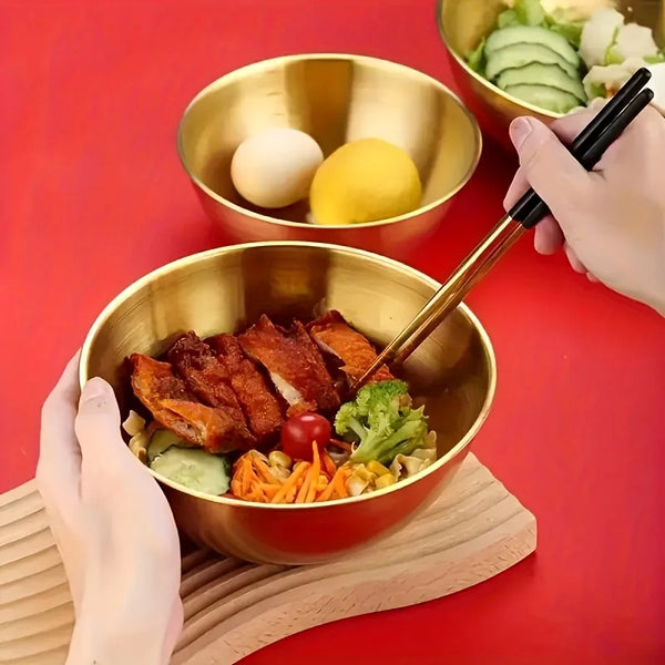 Eine Hand benutzt Chopsticks, um ein gelbes Ei aus einer goldenen Schale zu heben, mit einem Salat in einer anderen goldenen 