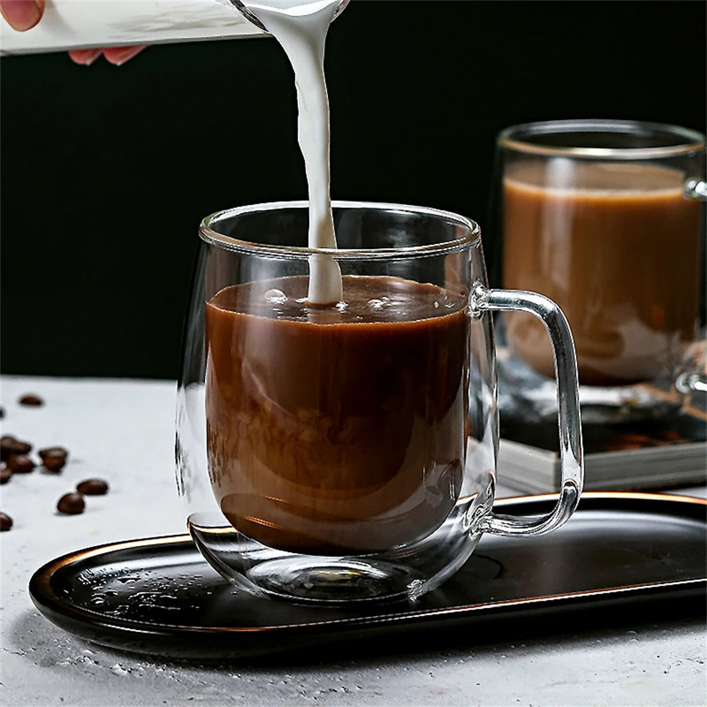 A close-up shot of a double wall insulated glass coffee cup being filled with milk from a pitcher.