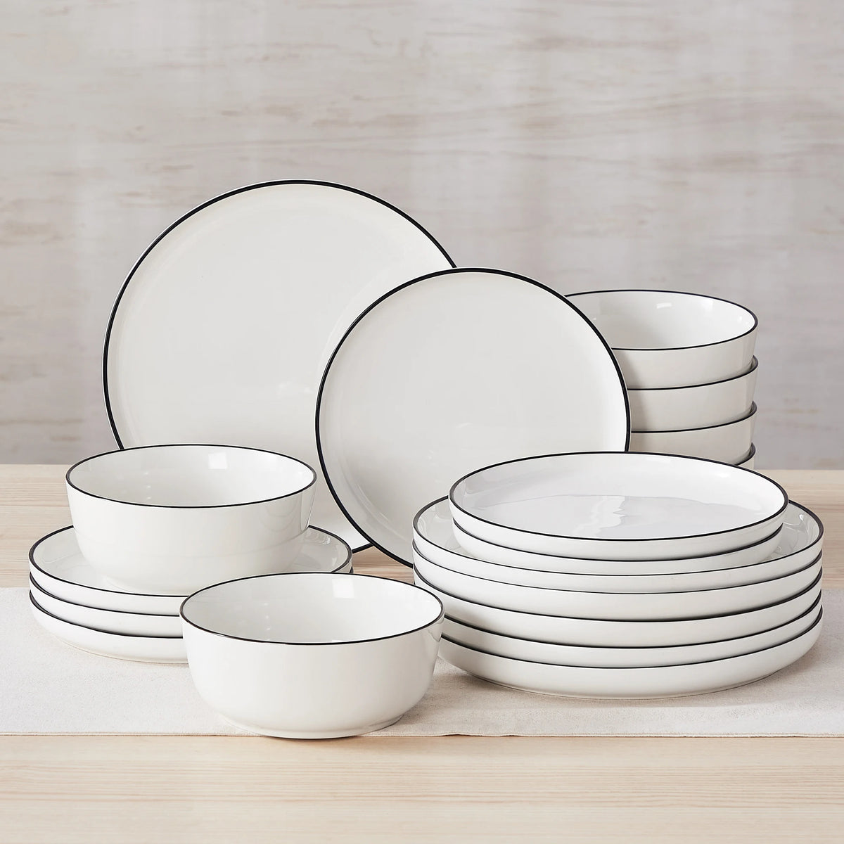 A stack of white porcelain dinnerware including plates and bowls with black rims on a wooden surface.