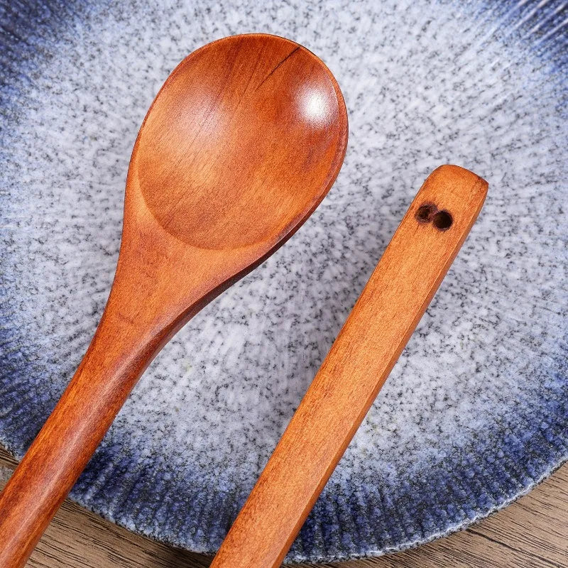 A pair of natural wooden serving spoons resting on a textured blue and white plate.