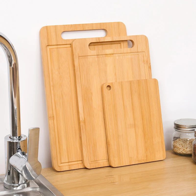 A set of three light wood bamboo kitchen cutting boards resting on a wooden countertop.