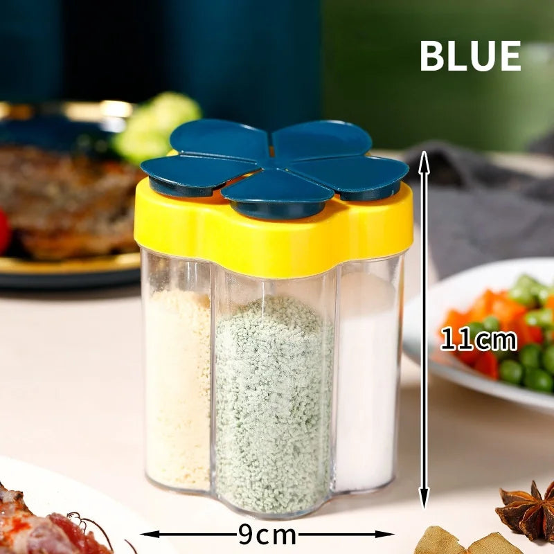 Frasco de condimentos con múltiples aberturas y tapas amarillas y azules, lleno de especias blancas y verdes, sobre una mesa.