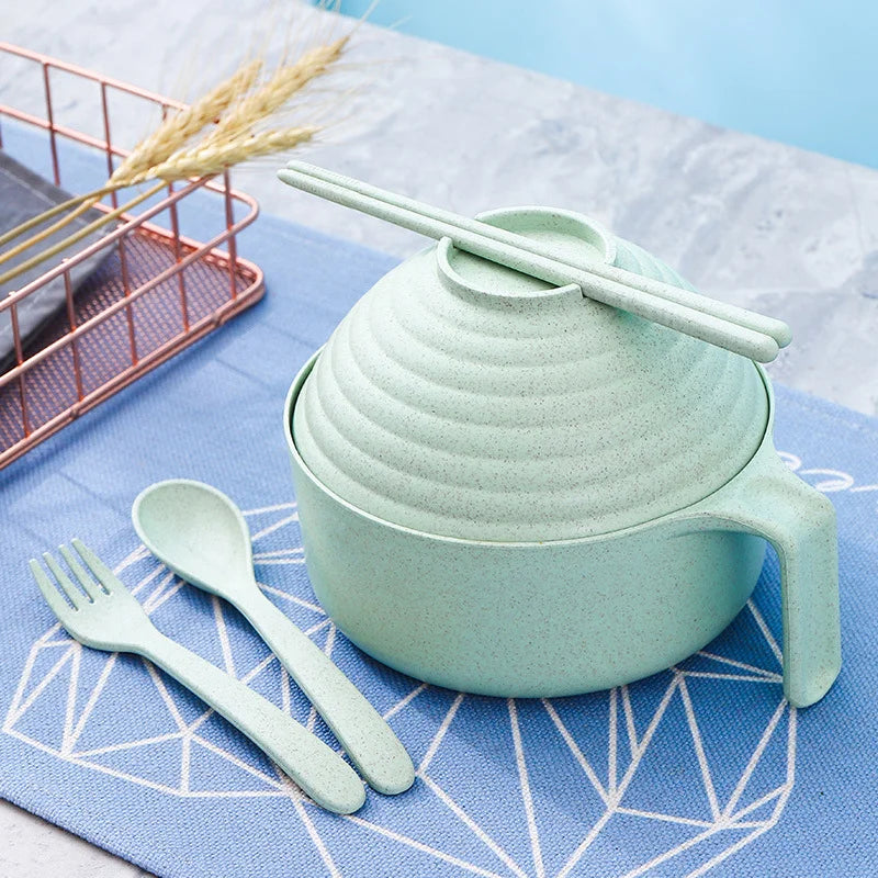 A light green microwave ramen cooking set with a lid and utensils resting on a blue cloth.
