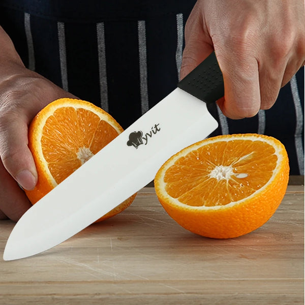Eine Hand hält ein weißes Keramik-Kochmesser mit schwarzem Griff neben einer geschnittenen Orange.