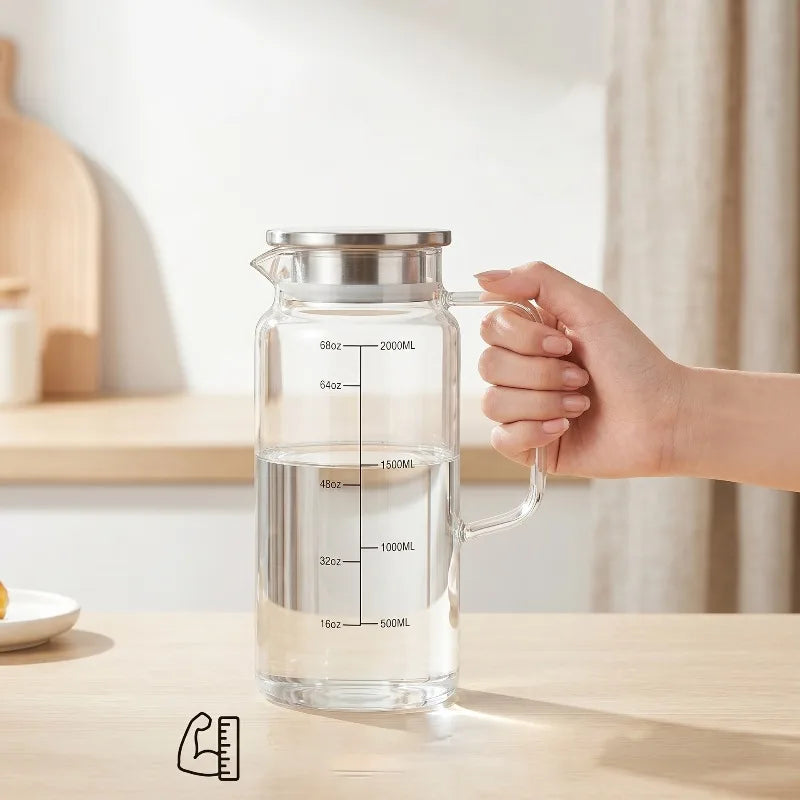 A hand is holding a clear glass water jug with a metal lid, demonstrating its volume markings.