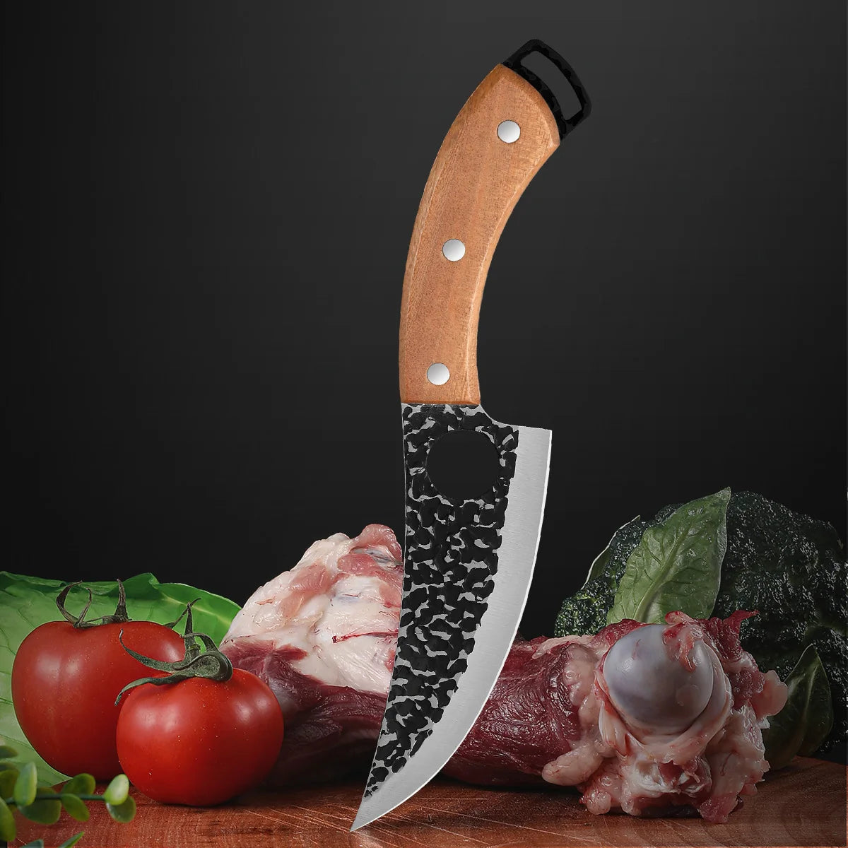A handmade forged kitchen knife set featuring a wooden handle and a large blade placed next to raw meat and tomatoes.