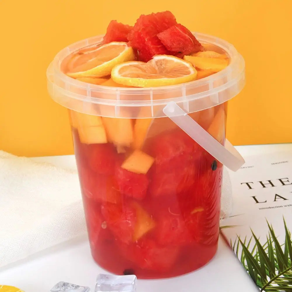 A clear plastic bucket filled with red fruit juice and orange slices, set against an orange background.