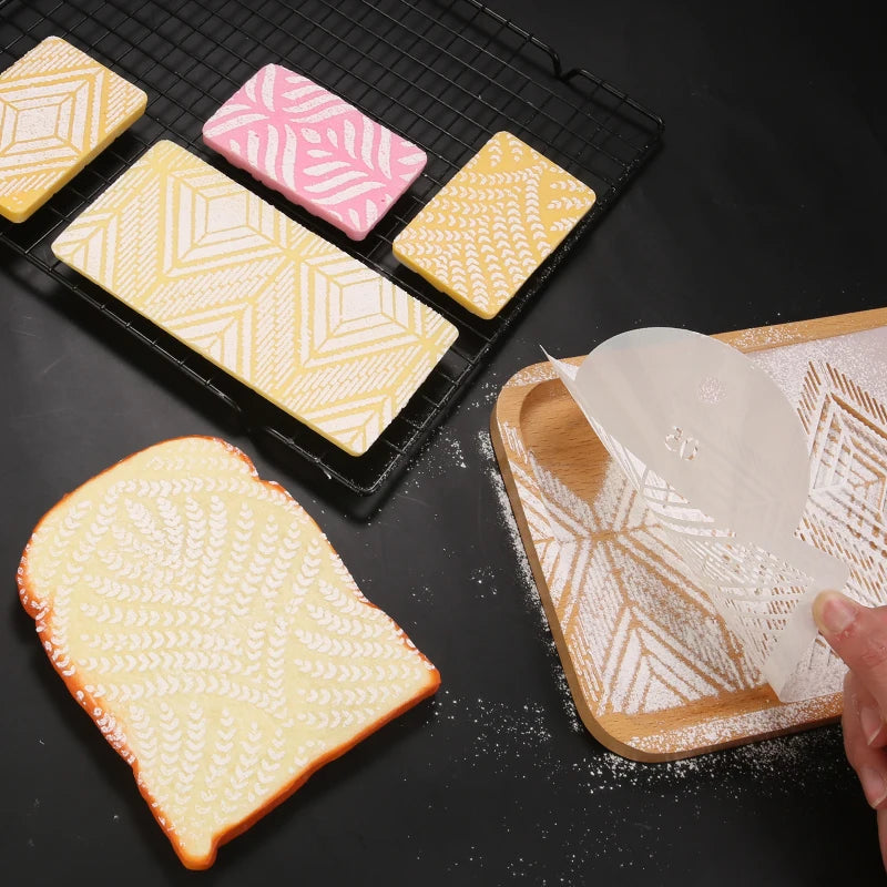 A set of plastic cake stencils and decorative tiles are displayed on a black cutting board.