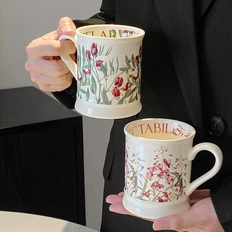 A white ceramic coffee mug with a floral design is held in a person's hand against a dark background.