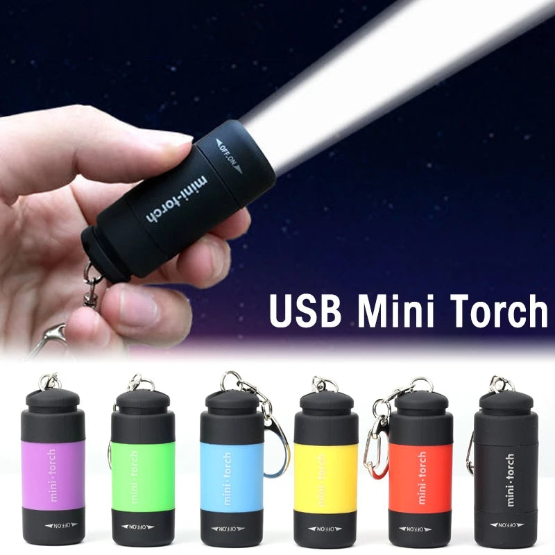 A hand holds a black USB Mini Torch flashlight and several versions of the mini torch keychain lights.