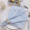 Una pila de servilletas de gasa de algodón azul claro reutilizables atadas con cinta de perlas sobre un plato blanco.