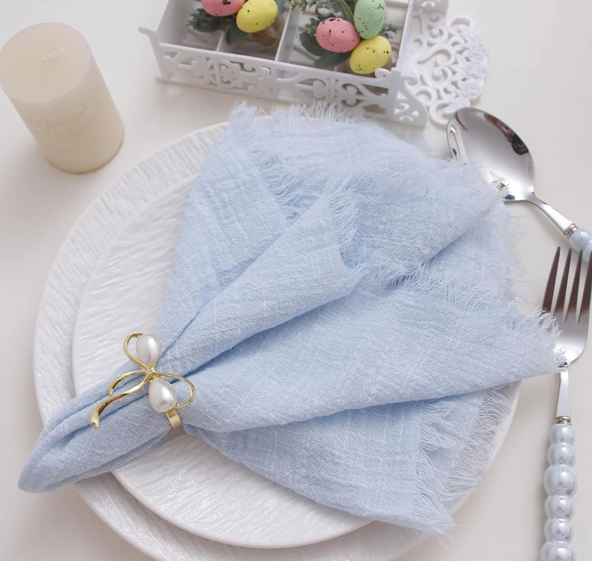 Una pila de servilletas de gasa de algodón azul claro reutilizables atadas con cinta de perlas sobre un plato blanco.