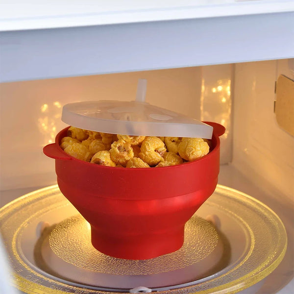 Rote Silikon-Popcornschüssel mit gelbem Popcorn auf einer Drehplatte in einem Mikrowellenherd.