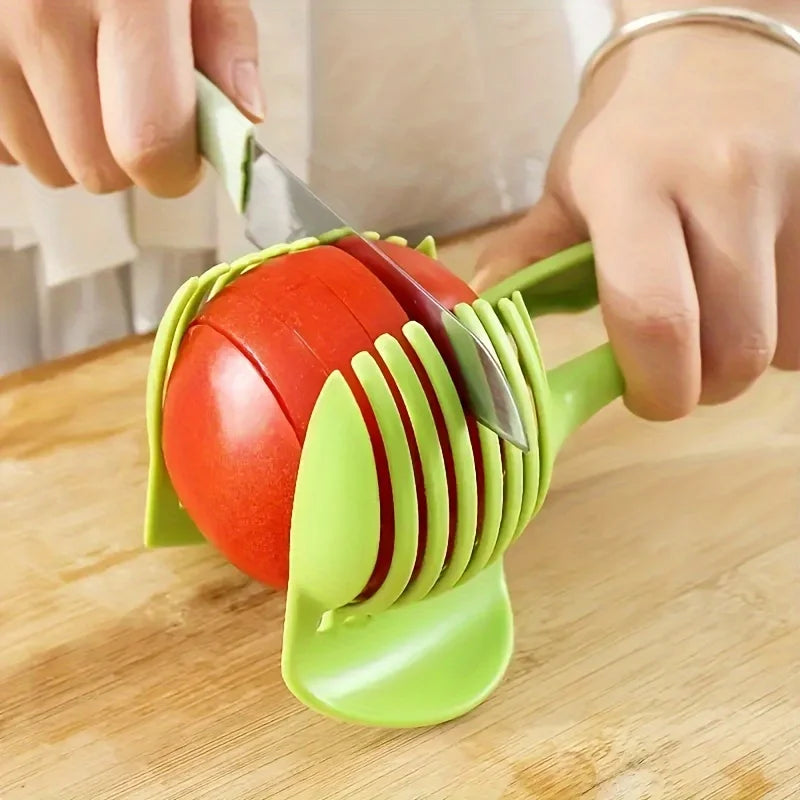 A hand is using a manual lemon and tomato slicer tool to cut a tomato on a wooden cutting board.