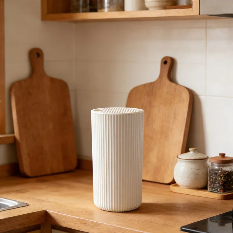 A white cylindrical knife block organizer stands on a wooden countertop next to a large wooden cutting board.