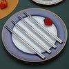 A set of reusable stainless steel chopsticks resting on a white plate with a strawberry on a purple plate.