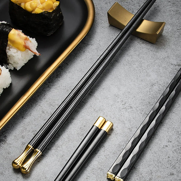 Ein Set aus fünf schwarzen und goldenen Legierung-Stäbchen für Sushi-Rollen auf grauer Oberfläche.