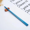 A pair of shiny blue stainless steel reusable chopsticks resting on a white surface next to a piece of paper.