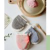 A set of striped and polka-dot insulated kitchen baking gloves resting on a white surface next to a wooden pot.