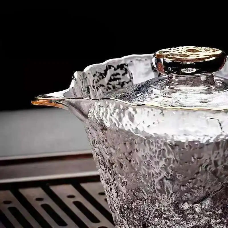 A close-up of an elegant glass teapot with a decorative lid, showing textured glass and a clear liquid.
