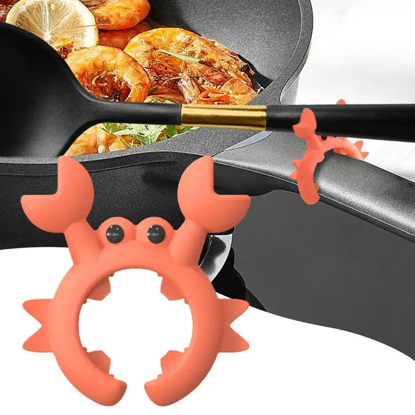 Orange krabbenförmiger Silikonlöffel und Spachtelhalter neben einer schwarzen Kochpfanne