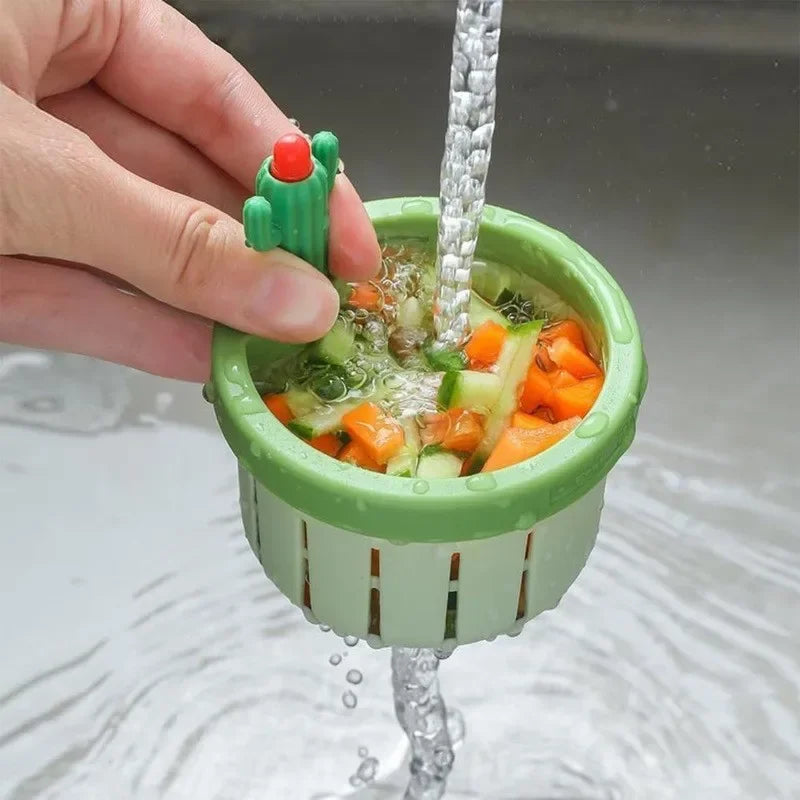 A hand holds a green cactus drain strainer, which is dripping water into a sink.