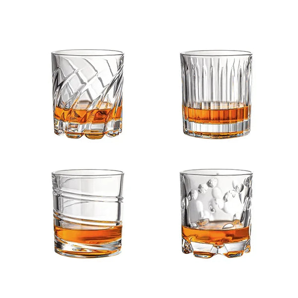 Ein Set aus vier klaren Whiskeygläsern, darunter ein strukturiertes Glas und ein Tumbler, gefüllt mit bernsteinfarbigem Flüss