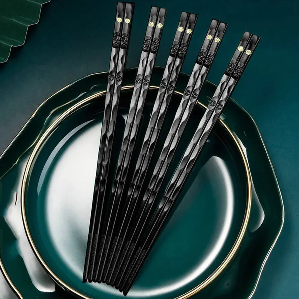 A set of black chopsticks with gold accents resting on a dark green plate.