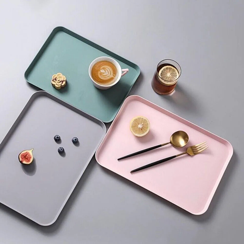 A pink rectangular serving tray holds a glass of juice and two spoons on a gray surface.