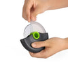 A hand is holding a black pizza dough slicing tool with a clear plastic blade and a green handle.