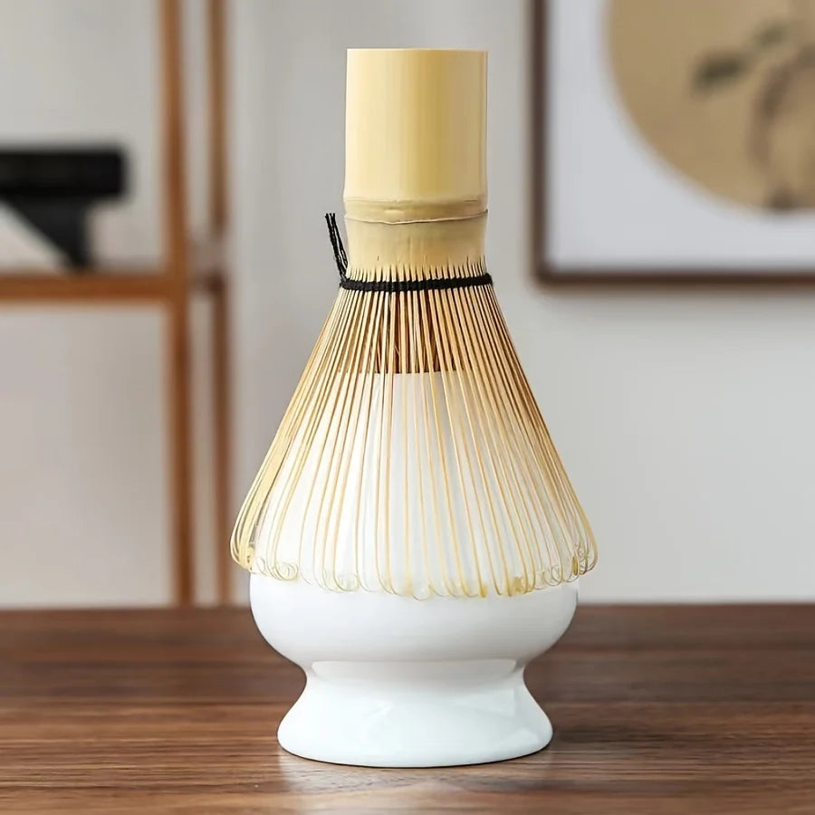 A set of natural bamboo tea tools with a light yellow handle and a delicate, fan-like structure resting on a white ceramic di