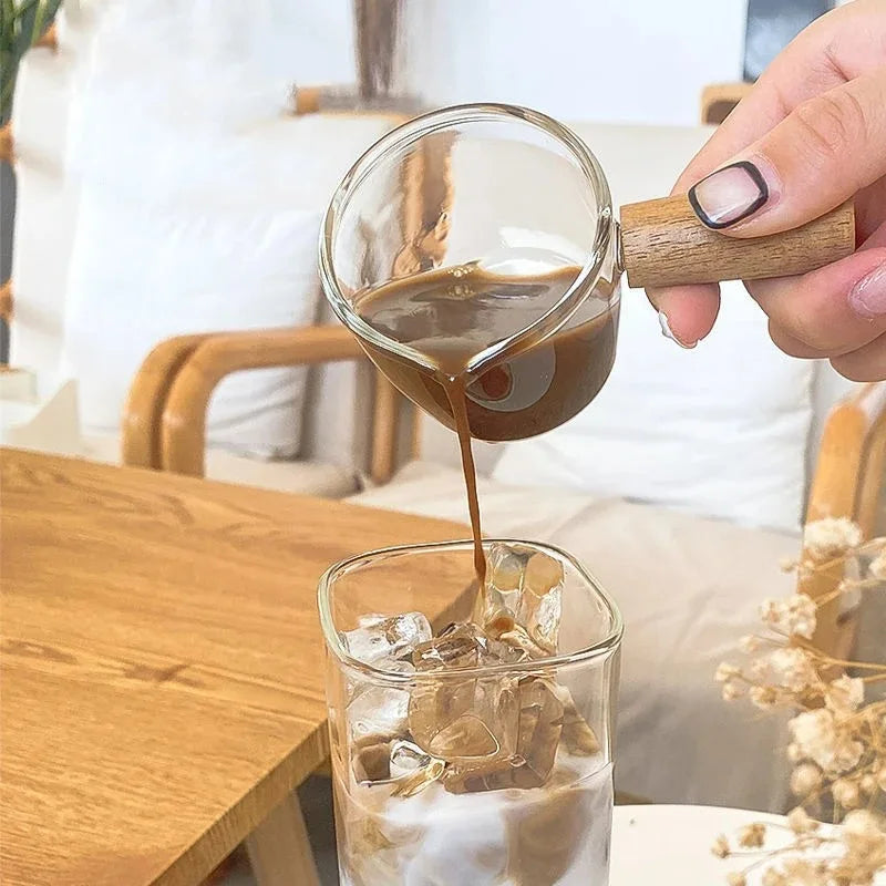 A hand pours a dark brown liquid from a glass into an ice-filled tumbler.