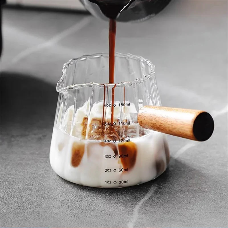 Una taza medidora de vidrio se está llenando de espresso de un dispositivo pour-over, demostrando varias medidas de líquido.