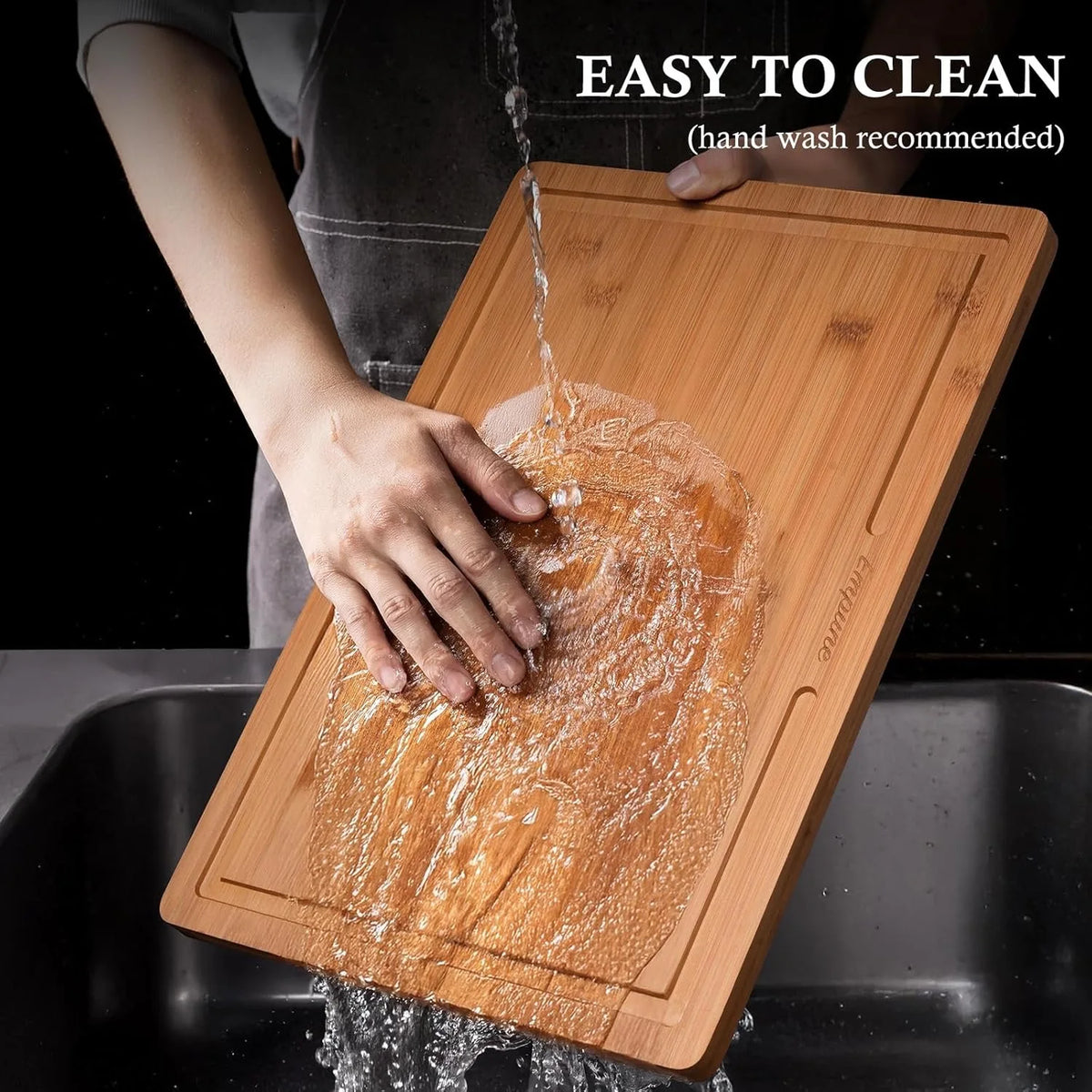 A hand is washing a wooden cutting board under running water, demonstrating its easy to clean feature.