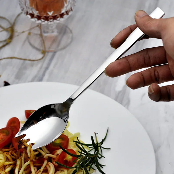 Eine Hand hält ein silbernes Edelstahl-Gemüseschöpflbesteckset auf einem weißen Teller mit Nudeln und Tomaten.