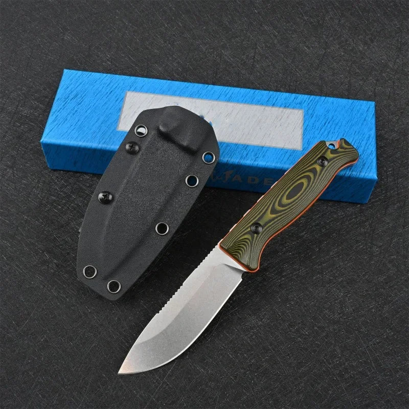 A black fixed blade outdoor camping knife with a green handle is placed on a dark surface next to a blue box.