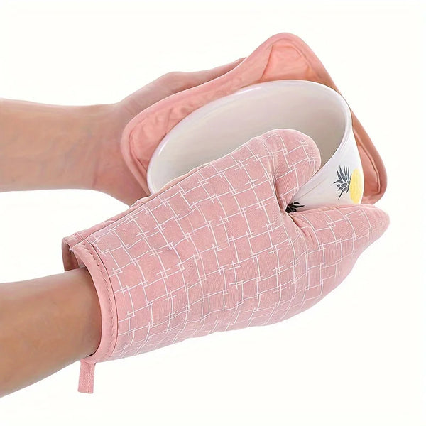 A hand is holding a pink heat-resistant oven glove and pot holder set with a white interior.