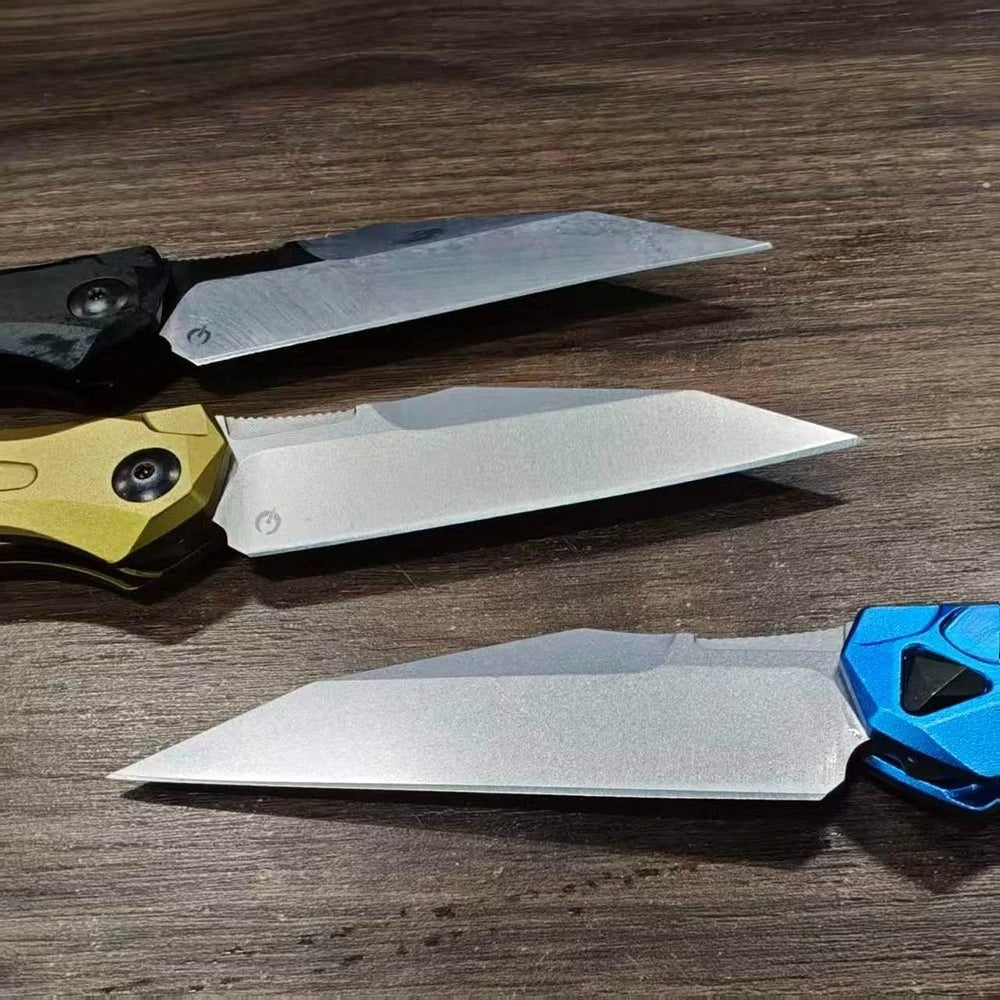 Three folding blade knives in black, yellow, and blue are displayed on a wooden surface.