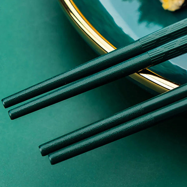 Ein Paar dunkelgrüner Chopsticks auf einem türkisen Teller mit goldenen Akzenten.
