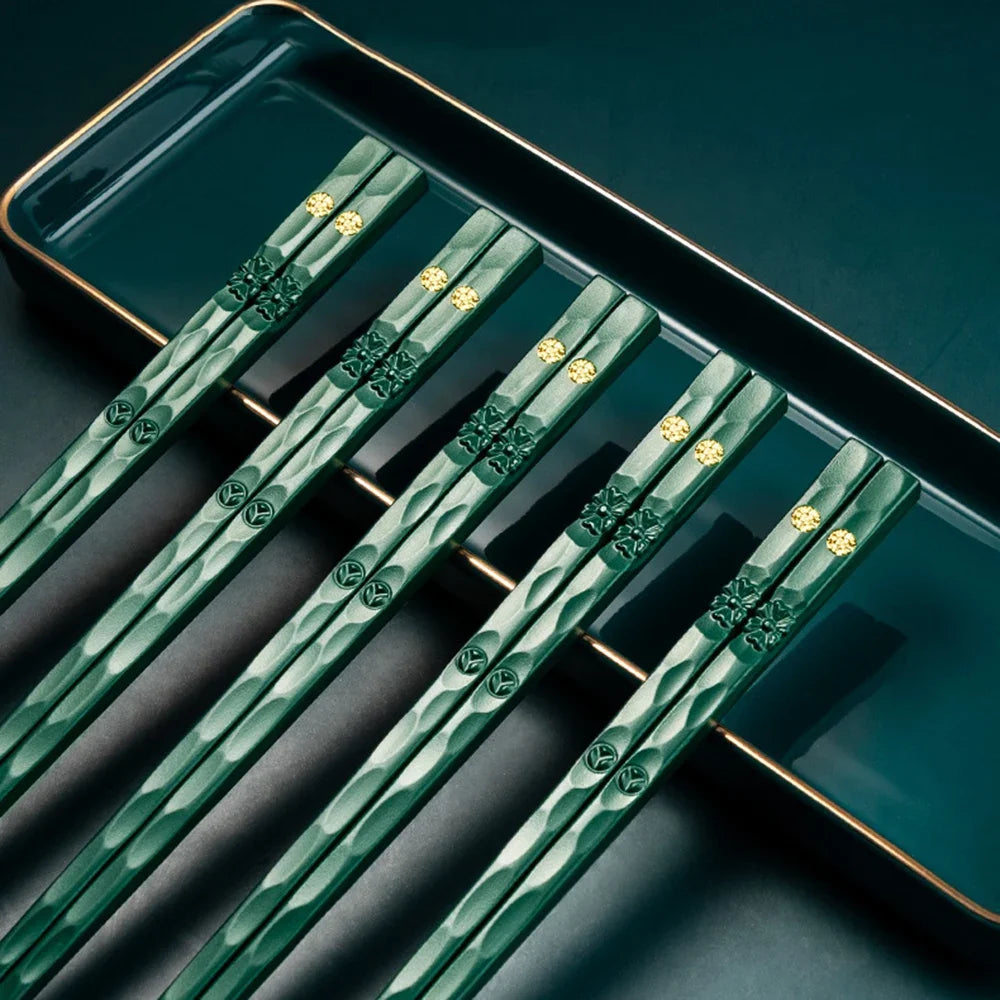A set of reusable multi-color chopsticks with green and gold accents displayed on a dark plate.