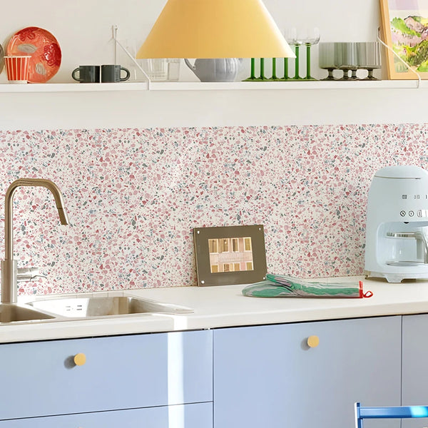 A kitchen countertop with a pink terrazzo wall decal backsplash, a faucet, and various kitchen items.
