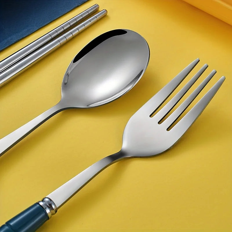 Juego de cubiertos de acero inoxidable (cuchara, tenedor y cuchillo) sobre una superficie amarilla junto a un cuaderno azul.
