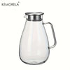 A clear glass pitcher with a metal lid and handle used for beverages.
