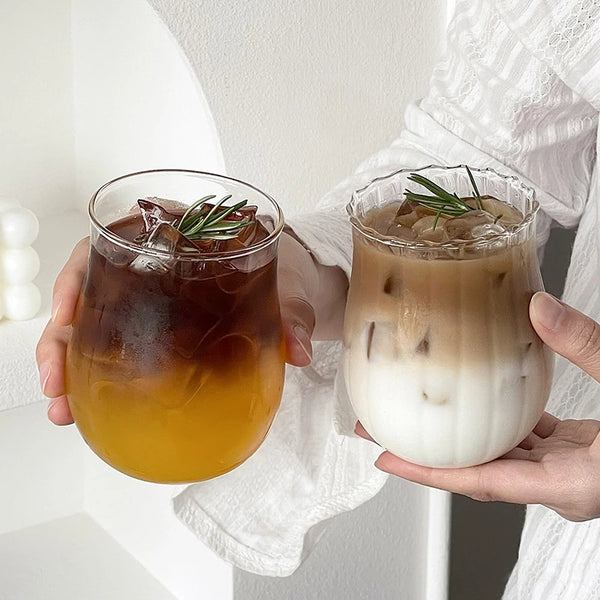 Eine Hand hält ein elegantes, durchsichtiges Glas mit Eiskaffee und Rosmarin-Garnitur.