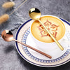 A set of gold and rose gold stainless steel coffee and tea spoons resting on a white cup and saucer.