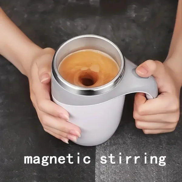 Hands hold a silver mug with a white base demonstrating magnetic stirring.